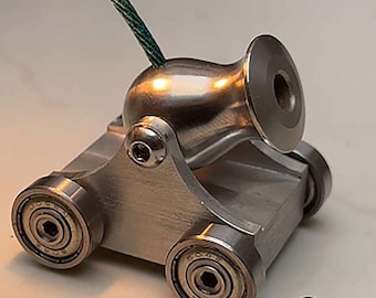 May include: A miniature silver-toned metal cannon mounted on a carriage with four ball-bearing wheels. A green fuse is inserted into the top of the barrel, and a small metal ball bearing sits on the surface in front of the cannon.