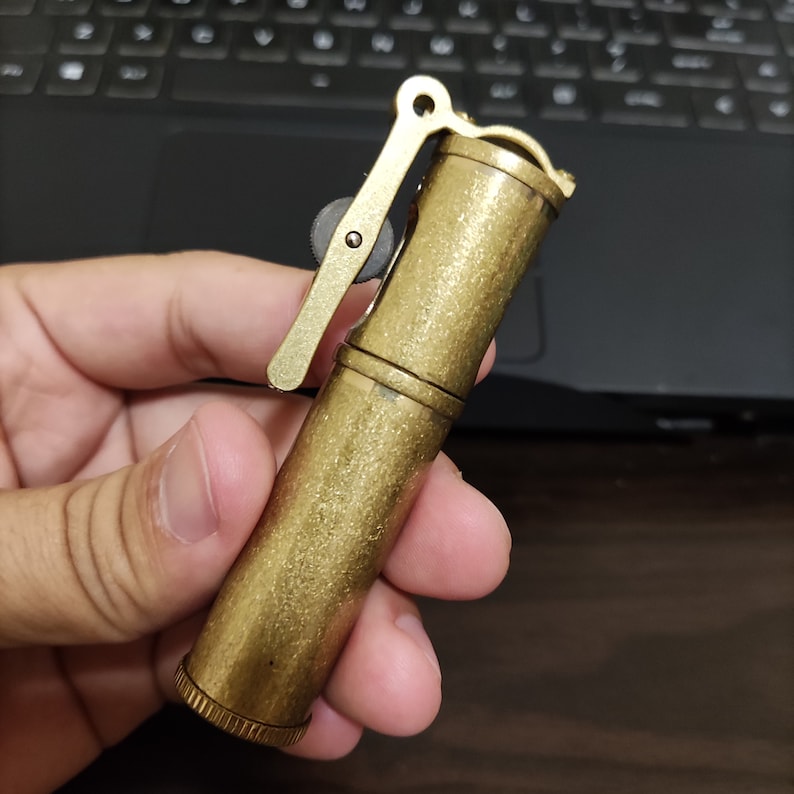 May include: A brass lighter with a textured finish and a lever on the side. The lighter is about 10 cm long.