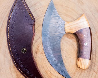 May include: A curved, Damascus steel knife with a wooden handle and a brown leather sheath. The blade has a distinctive pattern, and the handle features a combination of light and dark wood. The sheath is stitched with a decorative pattern.