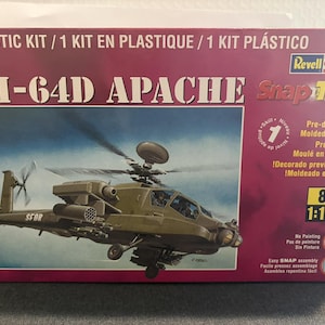 May include: A model kit box for an AH-64D Apache helicopter. The box is primarily red with the helicopter image in the center. The text "AH-64D APACHE Snap Tite" is prominently displayed. The kit is 1:100 scale and requires no painting.