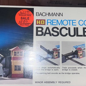 May include: A Bachmann HD Remote Control Bascule Bridge model train set. The box features a picture of a train crossing a bridge, with a red and orange sale sticker. The text on the box includes "Minor Assembly Required."