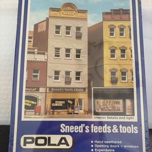 May include: A model kit box featuring a detailed miniature of a city street with buildings. The buildings are in various colors, including brick red, beige, and yellow. The storefronts read "Sneed's feeds & tools". The box reads "POLA".