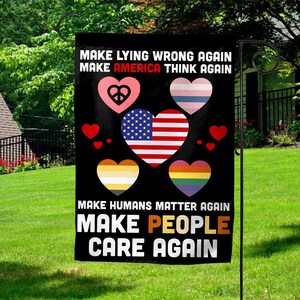 May include: A black garden flag with white text that reads "MAKE LYING WRONG AGAIN, MAKE AMERICA THINK AGAIN, MAKE HUMANS MATTER AGAIN, MAKE PEOPLE CARE AGAIN." The flag features hearts with various designs and colors.
