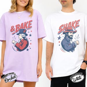 May include: A light purple t-shirt featuring a graphic of a historical figure in a red coat and top hat with the text & BAKE, and a white t-shirt featuring a graphic of a bearded figure in a red hat and blue coat with the text SHAKE.