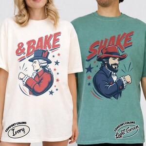 May include: Two short-sleeve t-shirts. The ivory shirt features a graphic of a historical figure in a red coat and hat with the text & BAKE. The light green shirt features a bearded figure in a blue coat and red hat with the text SHAKE.