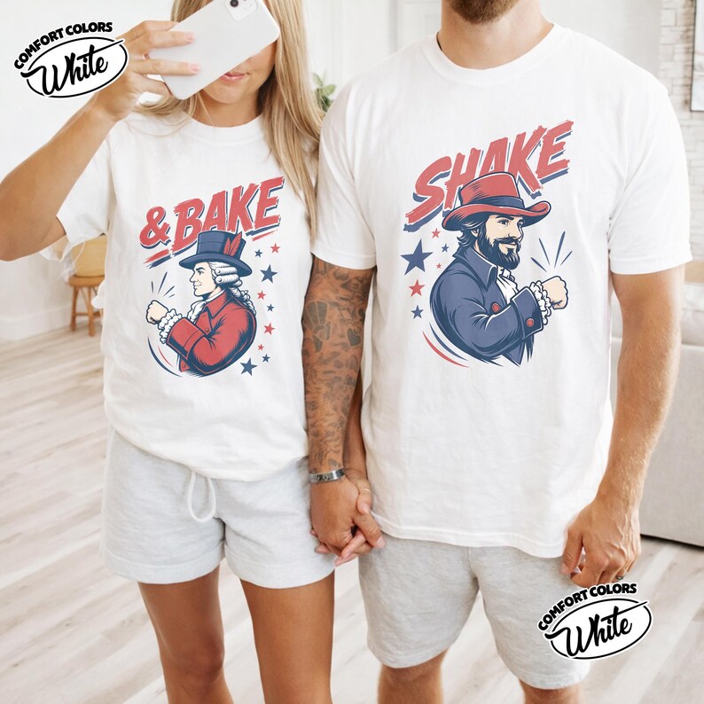 May include: Two white t-shirts featuring graphic prints. The left shirt displays a historical figure in a red coat and top hat with the text & BAKE. The right shirt shows a bearded figure in a blue coat and red hat with the text SHAKE.