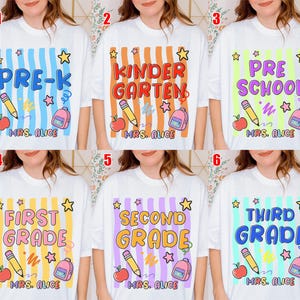 May include: A white t-shirt featuring six variations of a school-themed graphic. Each design includes a grade level, a pencil, an apple, a backpack, and stars over vertical stripes. The text "MRS. ALICE" is printed at the bottom of each graphic.