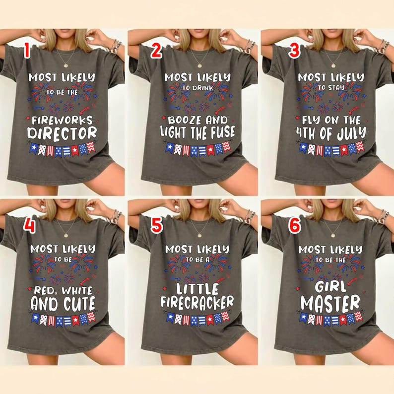 May include: A charcoal gray t-shirt featuring six variations of patriotic text and graphics. Each design includes red, white, and blue fireworks and bunting, with phrases like 'Most Likely to be the Fireworks Director' and 'Most Likely to be a Little Firecracker'.