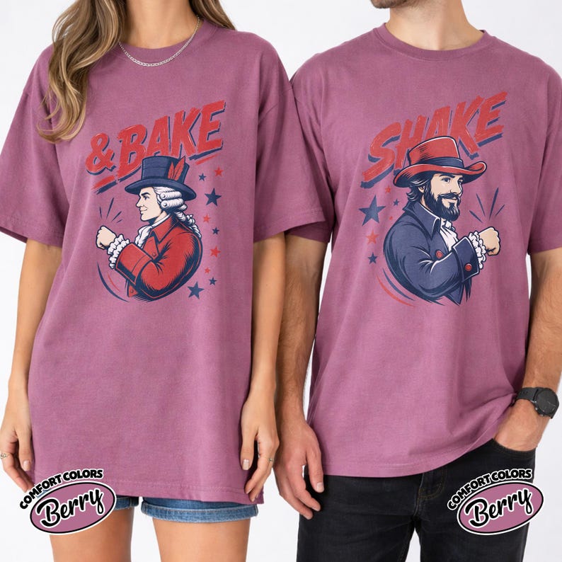 May include: Two berry-colored t-shirts featuring graphic prints. The left shirt displays a person in a colonial-style red coat and hat with the text & BAKE. The right shirt shows a person in a blue coat and hat with the text SHAKE.