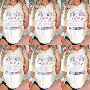 May include: A collection of six off-white short-sleeve t-shirts featuring red, white, and blue firework graphics and bunting. Each shirt displays unique text including Most Likely To Be The Fireworks Director, Booze, Stay, Cute, Firecracker, or Girl Master.