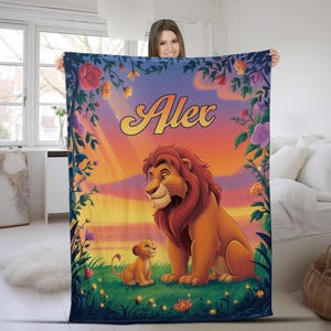 May include: A personalized blanket featuring a lion and cub illustration with the name "Alex" in a stylized font. The design includes a sunset backdrop, floral accents, and a vibrant color palette of orange, yellow, and blue.