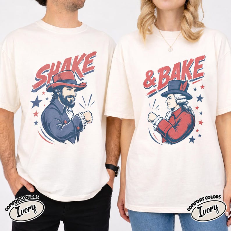 May include: Two ivory t-shirts featuring graphic prints. The left shirt displays a bearded figure in a red hat with the text SHAKE. The right shirt shows a figure in a colonial-style hat with the text & BAKE. Both designs include red and blue stars.