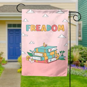 May include: A pink garden flag with the word "FREEDOM" in colorful letters. A stack of books with a bird on top is in the center of the flag.