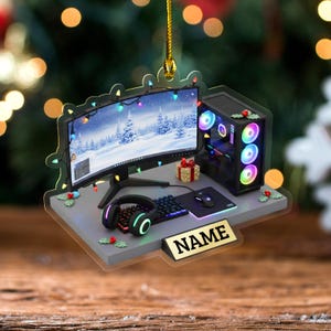 May include: A Christmas ornament featuring a gaming PC setup with a curved monitor displaying a winter scene. The setup includes a keyboard, mouse, and headset. The ornament has a gold string for hanging and a nameplate.