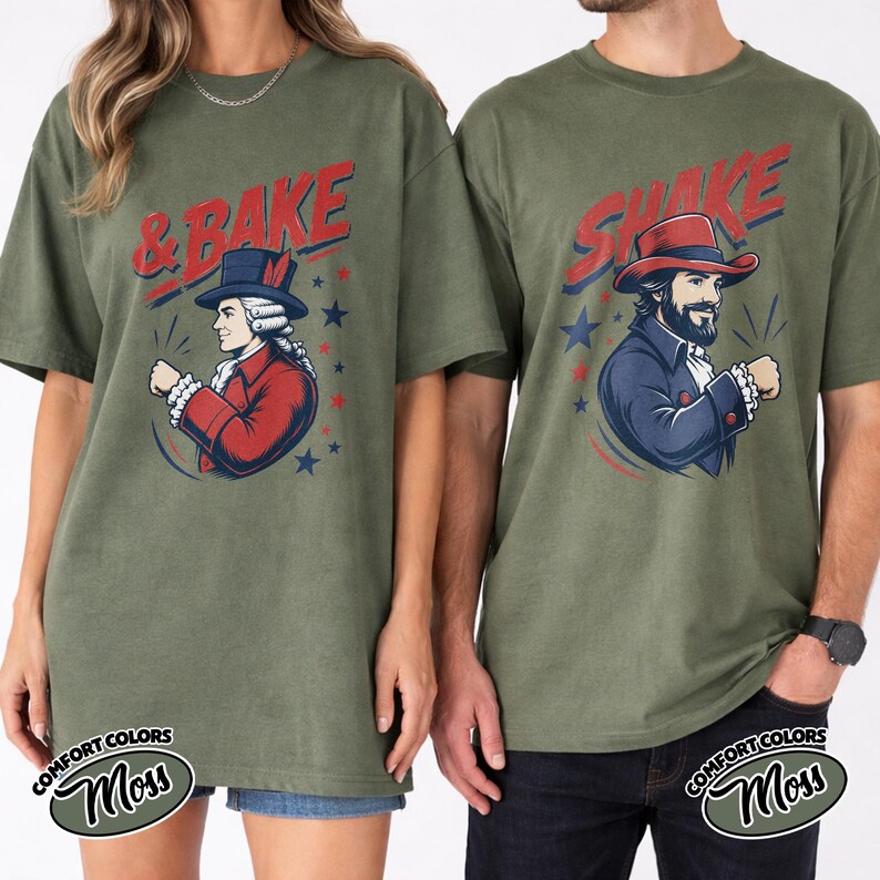 May include: Two olive green t-shirts featuring graphic prints. The left shirt displays a person in a red colonial coat and top hat with the text & BAKE. The right shirt shows a person in a blue colonial coat and top hat with the text SHAKE.