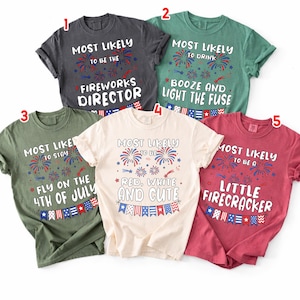 May include: Five short-sleeved crew neck t-shirts in charcoal, green, olive, cream, and red. Each shirt features red, white, and blue firework graphics, bunting, and text including Most Likely To Be The Fireworks Director, Booze, and Little Firecracker.
