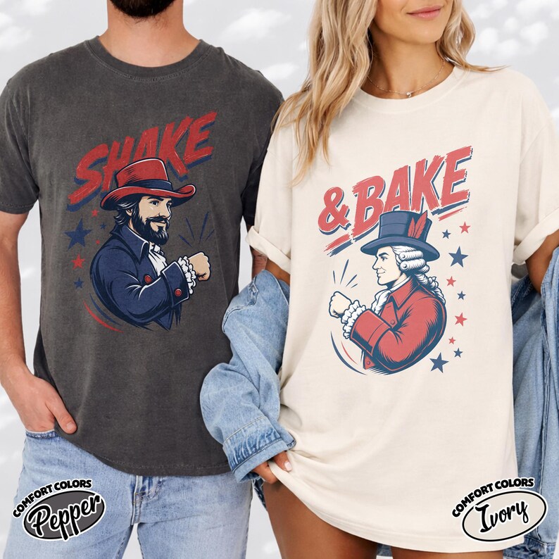 May include: A charcoal gray t-shirt with the red text SHAKE and a graphic of a man in a colonial hat, and an ivory t-shirt with the red text & BAKE and a graphic of a colonial figure in a hat, both featuring blue stars and red accents.