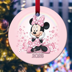 May include: A pink Christmas ornament featuring Minnie Mouse in a pink polka dot dress and bow. The ornament has a rainbow and floral design, with the name "Sarah" and the year "2025" printed on it. A red ribbon is attached for hanging.