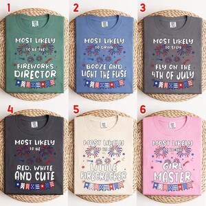 May include: A collection of six t-shirts in green, blue, dark gray, cream, and pink. Each shirt features red, white, and blue firework graphics, bunting, and text including Most Likely To Be The Fireworks Director, Booze, Stay, Red, White And Cute, Little Firecracker, or Girl Master.