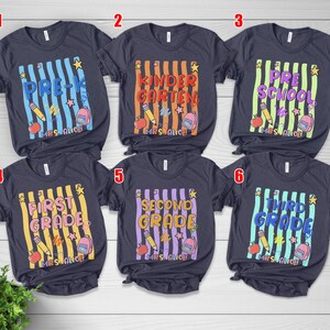 May include: Six dark gray short-sleeve t-shirts featuring school-themed graphics with vertical stripes, pencils, apples, backpacks, and stars. Each shirt displays a specific grade level from Pre-K to Third Grade and the personalized text Mrs. Alice.