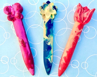 May include: Three colorful crayons shaped like flowers. The crayons are red, blue, and yellow with white swirls. The crayons are labeled "Crayola".