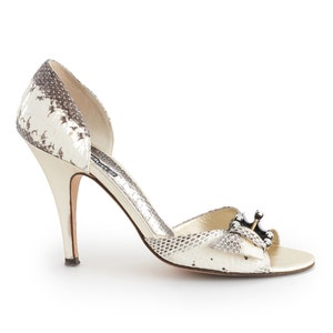 May include: White snakeskin heeled sandals with a peep toe and a jeweled buckle.