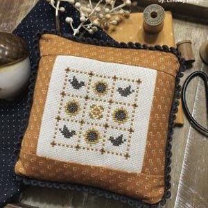 May include: A brown and white pillow with a nine-patch design featuring sunflowers and birds. The pillow has a black and white scalloped trim. The text "SEPTEMBER NINE PATCH" is at the top of the image and "PRIMROSE COTTAGE STITCHES" is at the bottom.