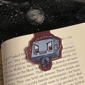 May include: A red, gray, and white robot bookmark with a menacing expression. The bookmark is made of paper and has a glossy finish. The robot has red eyes, a gray body, and a white antenna. The bookmark is designed to look like a robot from a cartoon or video game.