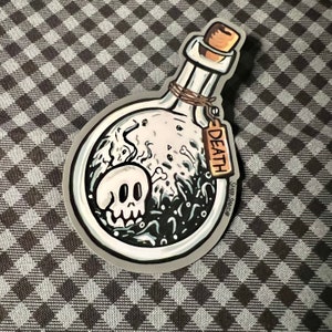 K&ouml;nnte beinhalten: Ein Aufkleber mit einer Cartoon-Illustration einer Zaubertrankflasche mit einem Totenkopf, Knochen und dem Wort "DEATH" auf einem Anh&auml;nger. Die Flasche hat einen Korken und ist mit Bindfaden gebunden. Der Aufkleber hat einen wei&szlig;en Rand.
