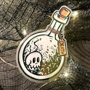 K&ouml;nnte beinhalten: Ein Aufkleber mit einer Cartoon-Illustration einer Zaubertrankflasche mit einem Totenkopf, Knochen und dem Wort "DEATH" auf einem Anh&auml;nger. Die Flasche hat einen Korken und ist mit Bindfaden gebunden. Der Aufkleber hat einen wei&szlig;en Rand und ist vor einem dunklen Hintergrund platziert.