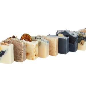 May include: Assortment of handmade soap bars in various colours and scents. The bars feature natural ingredients and decorative elements like dried flowers and citrus slices.