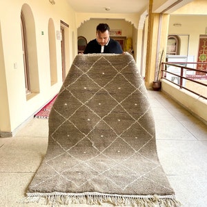 Peut inclure: Une personne tient un grand tapis rectangulaire brun et blanc avec un motif en losange. Le tapis a une bordure en franges.