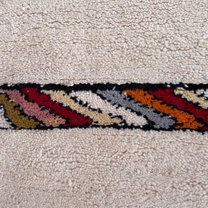 Puede incluir: Una alfombra blanca con un borde rayado de colores. El borde presenta una variedad de colores, incluyendo rojo, naranja, amarillo, verde, azul y negro.