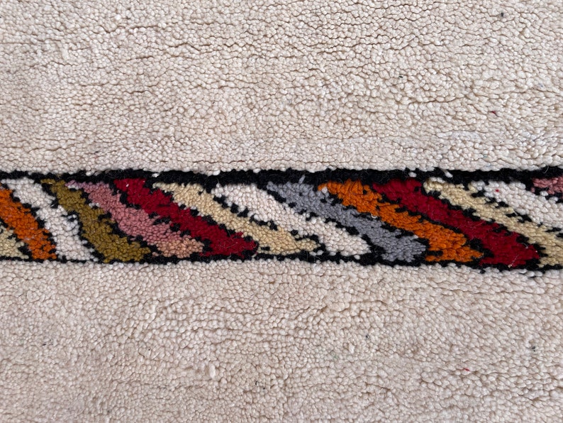 Puede incluir: Una alfombra blanca con un borde rayado de colores. El borde presenta una variedad de colores, incluyendo rojo, naranja, amarillo, verde, azul y negro.