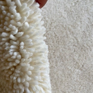 May include: Close-up of a white fluffy rug with a hand holding up a section of the rug to show the texture.