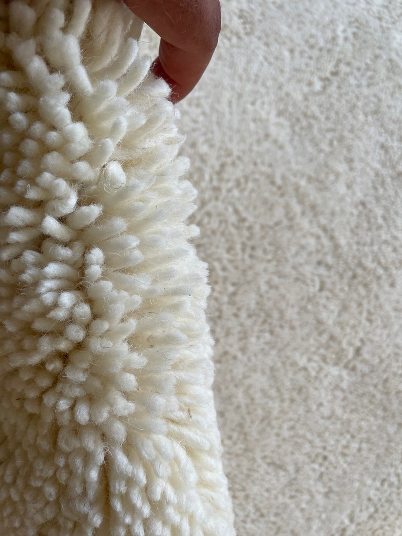 May include: Close-up of a white fluffy rug with a hand holding up a section of the rug to show the texture.