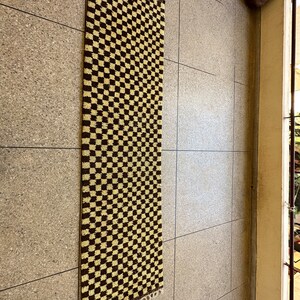 May include: A brown and beige checkered rug with a fringed edge. The rug is hanging on a wall.
