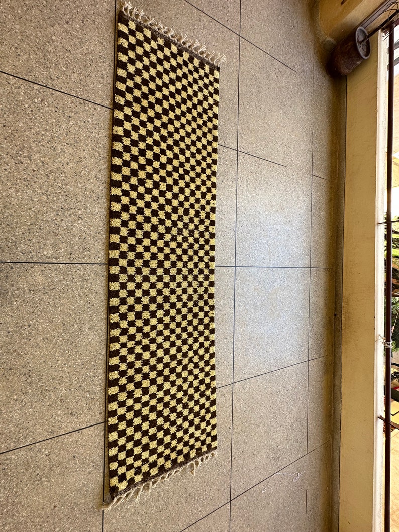 May include: A brown and beige checkered rug with a fringed edge. The rug is hanging on a wall.