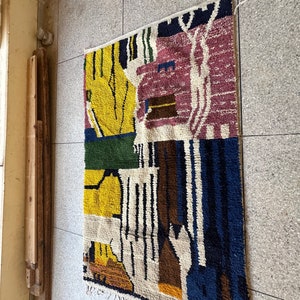 Puede incluir: Una alfombra abstracta colorida con formas geom&eacute;tricas en tonos de amarillo, azul, verde, marr&oacute;n y rosa. La alfombra tiene un fondo blanco y est&aacute; tejida con una variedad de texturas.