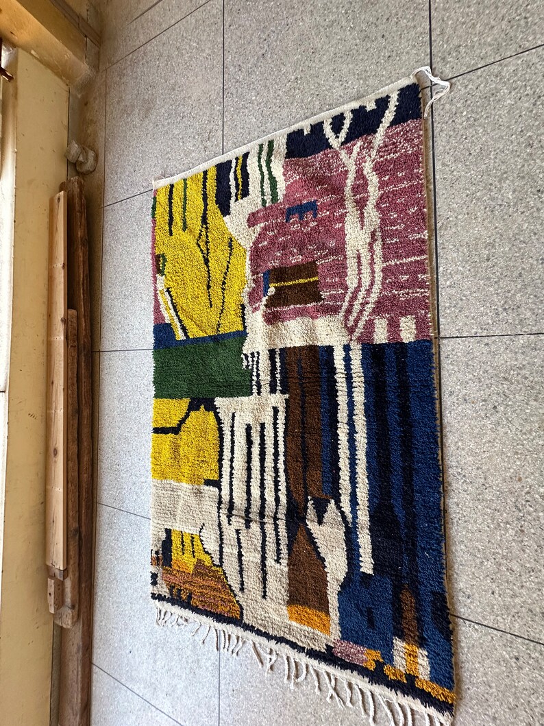 Puede incluir: Una alfombra abstracta colorida con formas geom&eacute;tricas en tonos de amarillo, azul, verde, marr&oacute;n y rosa. La alfombra tiene un fondo blanco y est&aacute; tejida con una variedad de texturas.