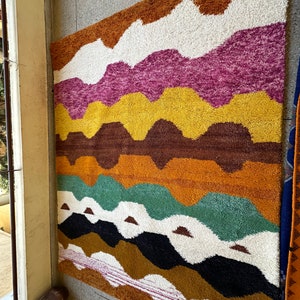 May include: A colorful rug with a wavy pattern in shades of brown, orange, yellow, pink, white, green, and black.