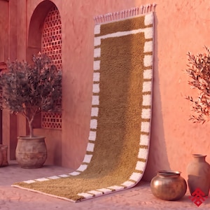 Peut inclure: Un long tapis de couloir rectangulaire doté d'un panneau central vert olive profond bordé d'un cadre épais à texture blanche et hirsute. Le tapis présente un bord supérieur à franges et une construction à poils denses et touffus.