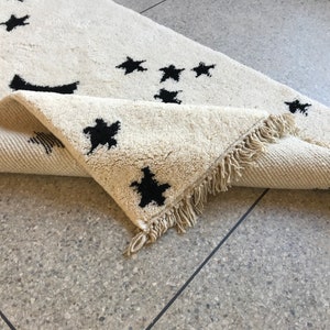 May include: A white rug with black star shapes woven into the fabric. The rug has a fringe border.