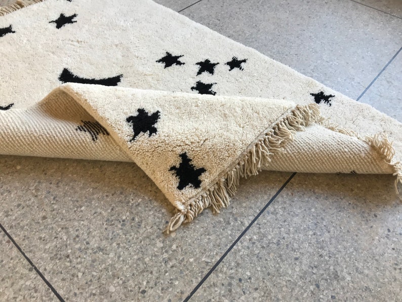 May include: A white rug with black star shapes woven into the fabric. The rug has a fringe border.