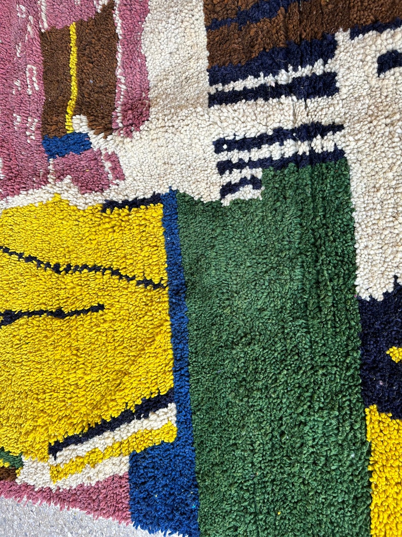 Puede incluir: Primer plano de una alfombra colorida con patrones geom&eacute;tricos en tonos de rosa, amarillo, verde, azul, blanco y marr&oacute;n. La alfombra est&aacute; hecha de un material suave y texturizado.