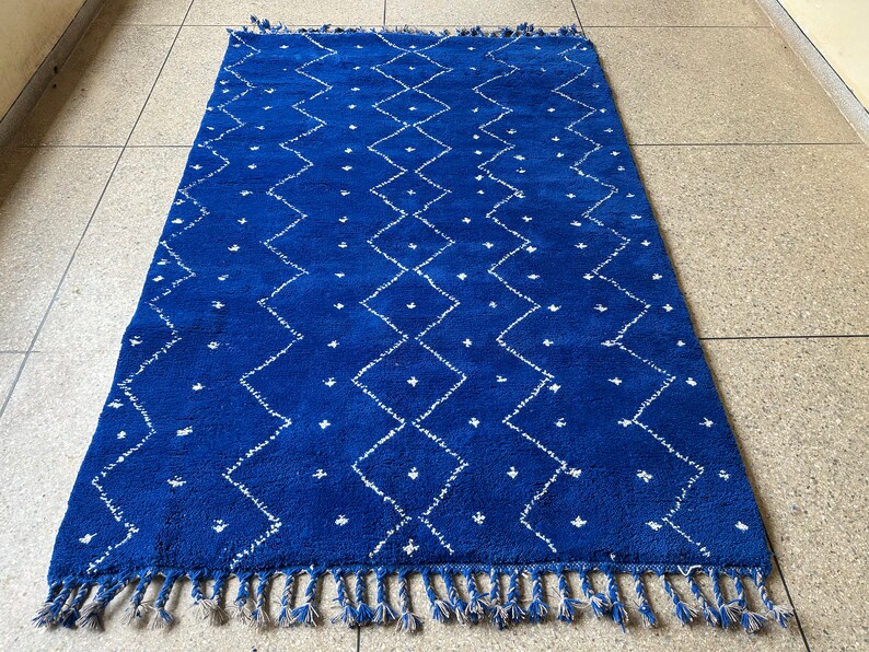 Puede incluir: Una alfombra marroqu&iacute; azul y blanca con un patr&oacute;n de diamantes y flecos.