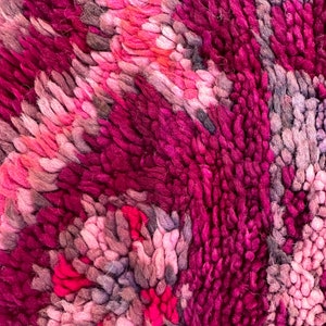 Pu&ograve; includere: Primo piano di un tappeto strutturato con un design astratto. Il tappeto presenta un mix di tonalit&agrave; rosa, magenta e grigie, creando una superficie visivamente ricca. Le fibre morbide sono fittamente impacchettate, suggerendo una consistenza morbida e confortevole.