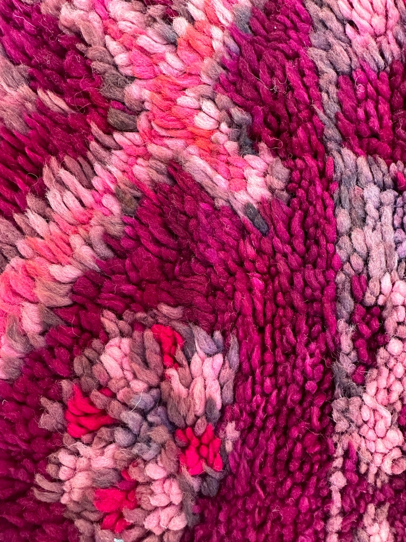Pu&ograve; includere: Primo piano di un tappeto strutturato con un design astratto. Il tappeto presenta un mix di tonalit&agrave; rosa, magenta e grigie, creando una superficie visivamente ricca. Le fibre morbide sono fittamente impacchettate, suggerendo una consistenza morbida e confortevole.