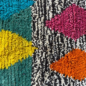 K&ouml;nnte beinhalten: Nahaufnahme eines bunten Teppichs mit geometrischem Muster. Der Teppich besteht aus verschiedenen farbigen Garnen, darunter Blau, Gr&uuml;n, Gelb, Rosa, Orange, Schwarz und Wei&szlig;.