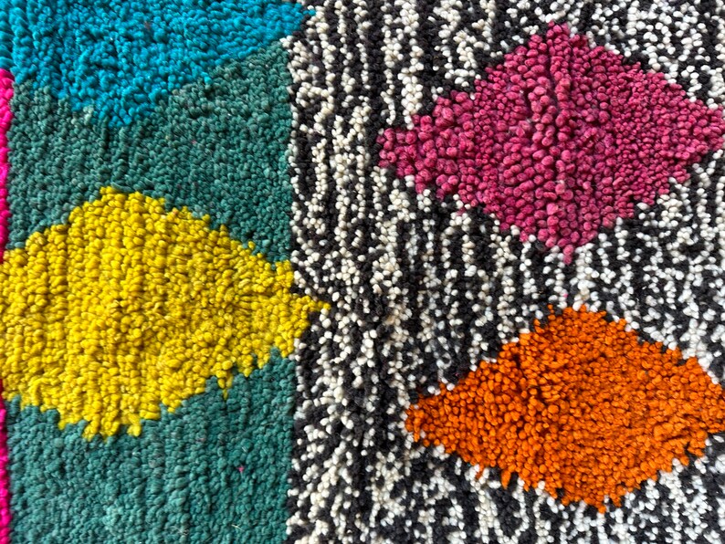 K&ouml;nnte beinhalten: Nahaufnahme eines bunten Teppichs mit geometrischem Muster. Der Teppich besteht aus verschiedenen farbigen Garnen, darunter Blau, Gr&uuml;n, Gelb, Rosa, Orange, Schwarz und Wei&szlig;.
